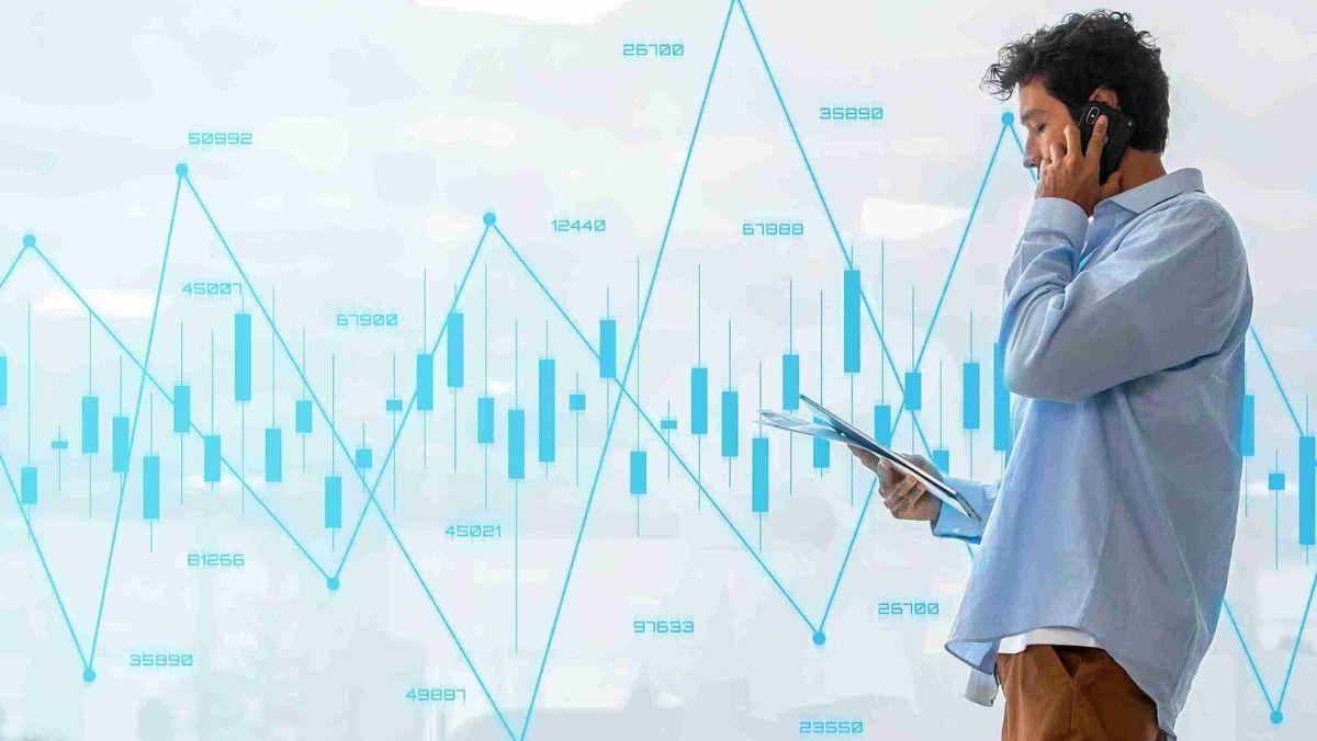 A man reviewing documents while talking on the phone, surrounded by blue colored trading charts